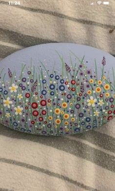 a painted rock sitting on top of a bed covered in green grass and wildflowers