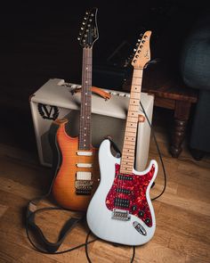 two electric guitars sitting on top of a hard wood floor next to an amp guitar