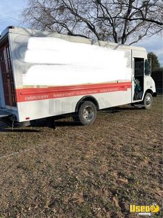 a white and red trailer parked on top of a dry grass field next to a tree