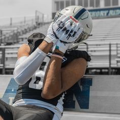 a football player sitting on the sidelines with his hands behind his head and wearing a helmet