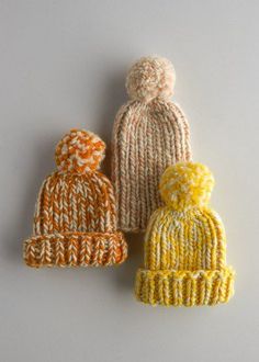 three knitted hats sitting next to each other on top of a gray surface,