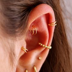 a woman wearing three different types of ear piercings on her left ear and the other one is gold