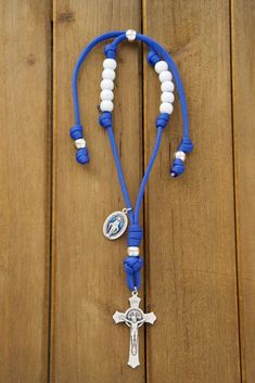 a blue and white necklace with a silver cross on the end is laying on a wooden surface