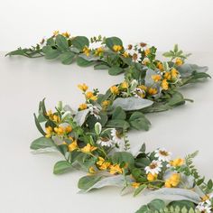 some yellow and white flowers are next to green leaves on a white surface with space for text