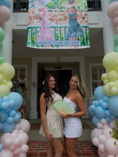 two beautiful young women standing next to each other in front of a building with balloons