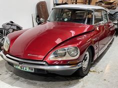 a red car parked in a garage next to a pile of junk on the floor