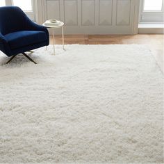 a blue chair sitting on top of a white rug in a living room next to a window