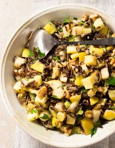 a bowl filled with rice and vegetables on top of a white table cloth next to a spoon