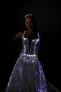 a woman in a dress that is lit up with purple and blue lights, standing against a black background