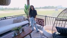 a woman standing on top of a balcony next to a white couch and wooden table