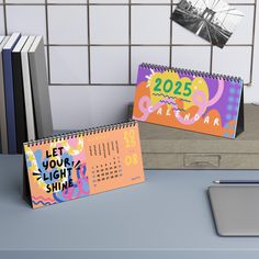 two calendars sitting on top of a desk next to a laptop computer and books