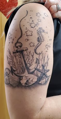 a woman's arm with an anchor and seahorse tattoo on it, in front of a wooden wall