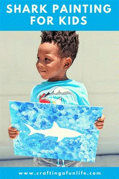 a young boy holding up a shark painting with the words shark painting for kids on it