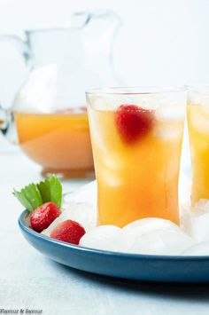 two glasses filled with ice and strawberries on a plate next to another glass pitcher