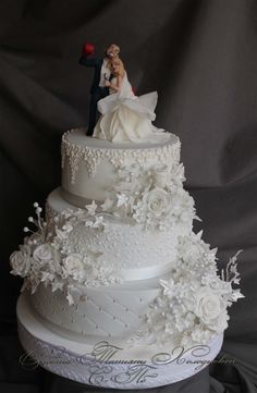 a wedding cake with white flowers and a bride and groom figurine on top