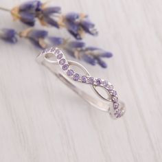 an image of a ring with purple stones on it and lavender flowers in the background