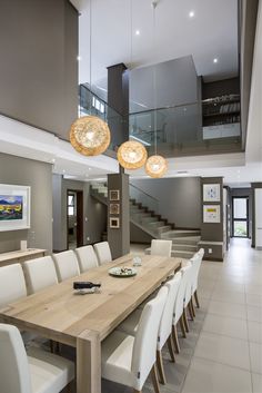 a dining room table with white chairs and lights hanging from it's ceiling in front of stairs