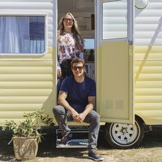 a man and woman sitting in the doorway of a yellow trailer