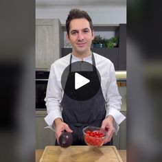 a man in an apron is holding a bowl with strawberries on it while standing next to a cutting board