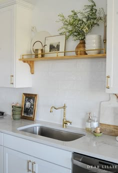 a kitchen with white cabinets and gold trim on the shelves above the sink is decorated with greenery