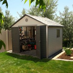 a small shed with bicycles in it on the grass next to a fence and trees