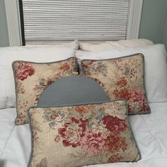 two pillows on top of a bed with white linens and floral print pillow cases