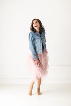 a woman in a pink tulle skirt and denim jacket laughing at the camera with her hands on her hips