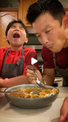 a father and son eating food together in the kitchen with an excited look on their face