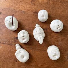 five white clay faces on a wooden table with a toothpick in the middle