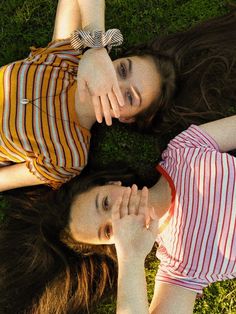 two young women laying on the grass with their arms around each other's shoulders