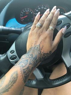 a woman's hand on the steering wheel of a car, with tattoos on her arm