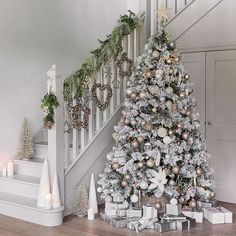 a white christmas tree with silver and gold ornaments in front of a bannister