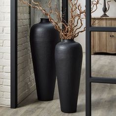 two large black vases sitting next to each other on top of a wooden floor