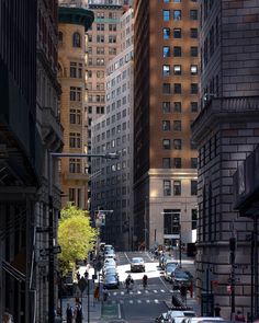 a city street filled with lots of tall buildings next to traffic and people walking on the sidewalk