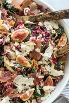 a white bowl filled with lots of different types of food and two wooden spoons