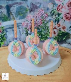 three decorated cake pops sitting on top of a white plate next to pink and blue flowers