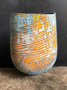 an orange and blue vase sitting on top of a stone counter next to a black wall