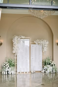 a wedding ceremony setup with white flowers and candles in front of a large gold framed sign