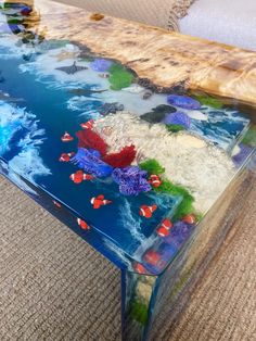 a glass coffee table with fish and corals painted on the top, sitting on carpeted flooring