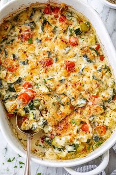 a casserole dish with spinach, tomatoes and cheese in it on a marble surface