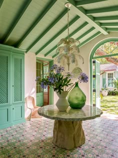 a green vase sitting on top of a table next to a white chair and doorway