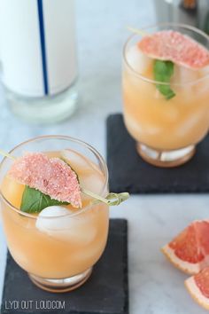 two glasses filled with grapefruit and garnish on top of coasters