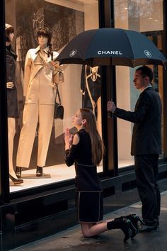 a woman standing next to a man holding an umbrella in front of mannequins