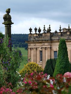 a large building surrounded by lots of flowers and trees in the foreground with a statue on top of it