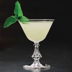 a glass filled with liquid and a green leaf on the rim, sitting on a black surface