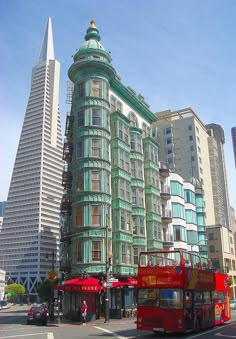 a red double decker bus driving down a street next to tall buildings in the city