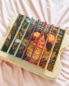 a wooden tray with six books on it sitting on top of a pink bed sheet