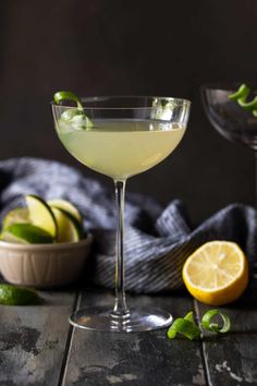 two martini glasses filled with white wine and garnished with limes, sitting on a wooden table