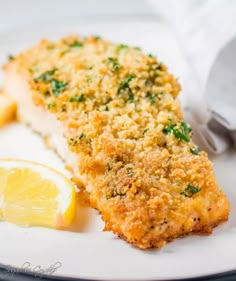 a piece of fish on a plate with lemon wedges and parmesan bread