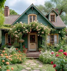 a green house with lots of flowers around the front door and steps leading up to it